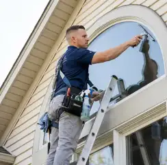 Professional window cleaner on a ladder using a squeegee to clean an exterior arched window, Orange, CA.